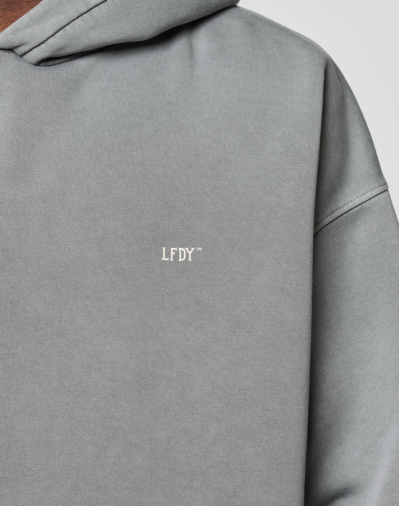 Close-up of the Basic Evidence Hooded by LIVE FAST DIE YOUNG, a gray oversized hoodie featuring white embroidered LFDY™ on the chest. The image showcases its textured fabric, minimal design, and subtle faded look.