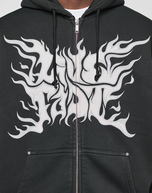 Someone wears the LFDY Inferno Hooded Zip by LIVE FAST DIE YOUNG, featuring an oversize fit, black individuelle Wascheffekt, zipper and drawstrings, plus bold Live Fast flame-like prints in white on the front and sleeves.