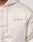 Close-up of a person wearing the LFDY Winter Bomber Jacket by LIVE FAST DIE YOUNG, a light beige oversized jacket with drawstring hood (Kapuze) and Live Fast cursive embroidery on the left chest. Partially visible zipper adds detail.