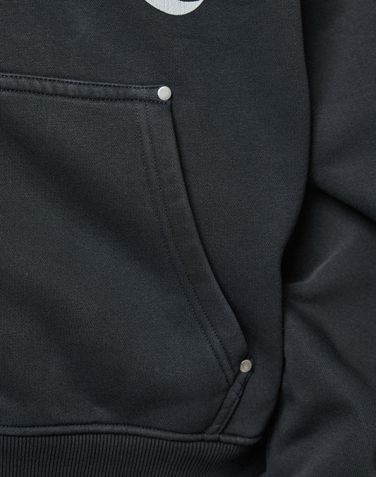 Close-up of the black LFDY Inferno Hooded Zip by LIVE FAST DIE YOUNG, showing its oversize pocket with visible stitching and three metallic rivets. The edge of a white front print hints at the individueller Wascheffekt on the fabric.