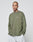 A person with a shaved head and tattoos wears the oversized LIVE FAST DIE YOUNG Basic Longsleeve in olive green (100% Baumwolle) and light gray pants, standing with hands in pockets against a plain light gray background.