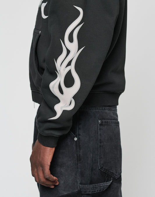 Someone wearing the LIVE FAST DIE YOUNG LFDY Inferno Hooded Zip with a bold white flame print on the front and sleeves, paired with dark denim jeans and shown in a side view.