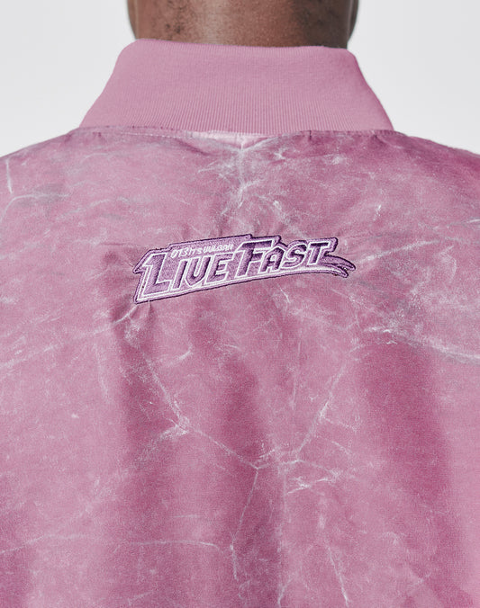 A close-up of the Washed Bomber Jacket by LIVE FAST DIE YOUNG shows pink marbled fabric and LIVE FAST embroidered in white and purple near the collar, finished with a subtle vintage wash for a sporty retro look.