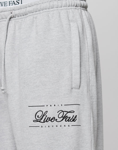 Close-up of the Wide Cuff Jogger by LIVE FAST DIE YOUNG in light grey French Terry, featuring a wide fit, elastic waistband, side pocket, and "PARIS LIVE FAST DIE YOUNG" text in black on the left thigh.