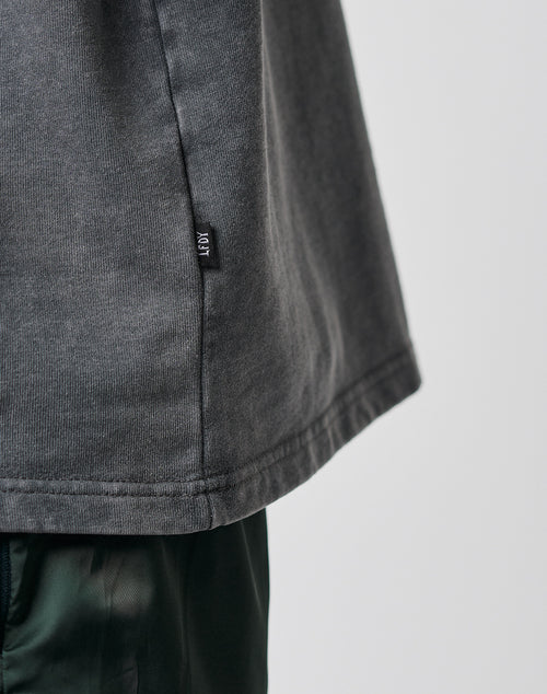Close-up of the lower side of the LIVE FAST DIE YOUNG Basic Heavy Longsleeve in dark gray, Regular Fit French Terry with a small black tag, worn over dark green pants against a plain light background.