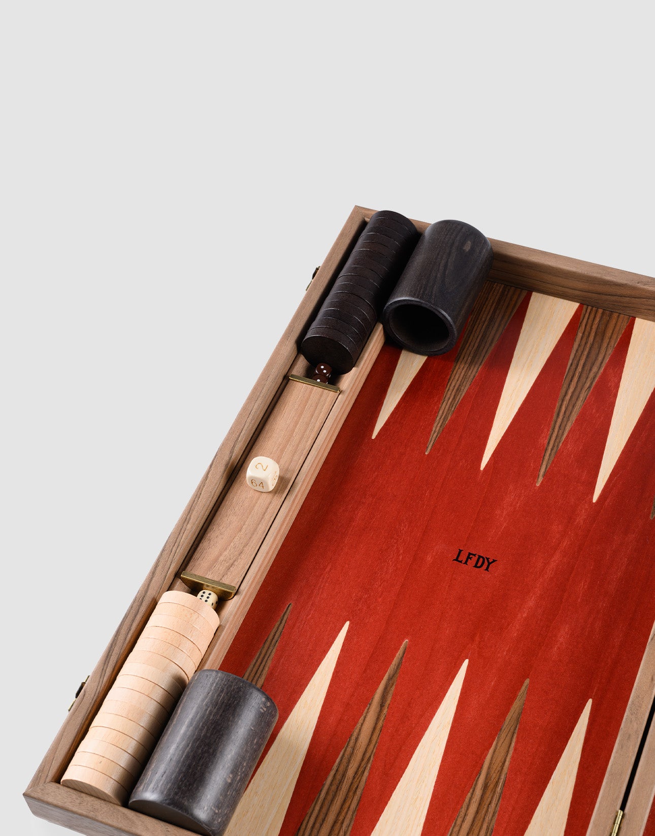 A close-up of the LFDY Backgammon by LIVE FAST DIE YOUNG, handcrafted in Greece from rich walnut wood, featuring red and wood-toned points, stacked pieces, two dice, a doubling cube, and stylish dark dice cups.