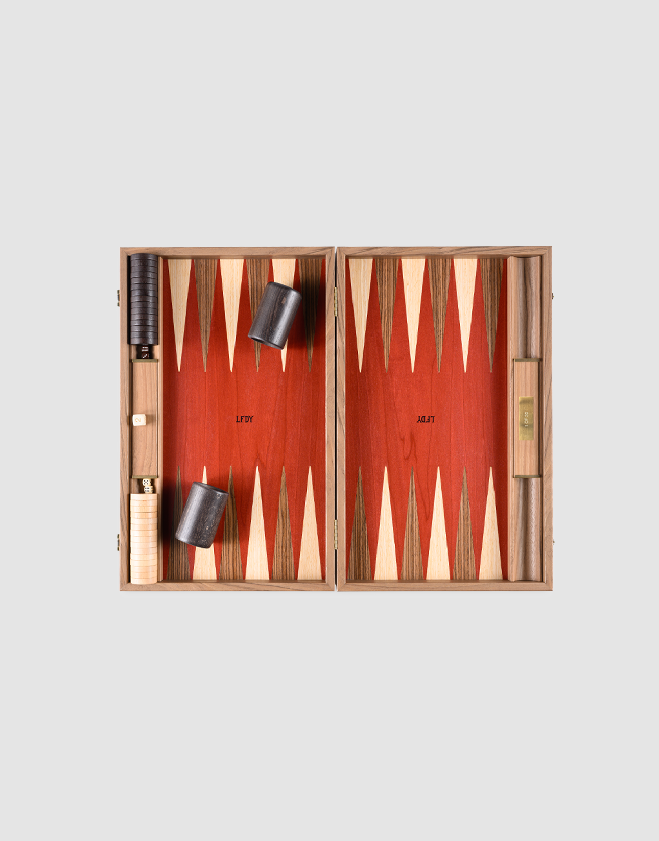 The LFDY Backgammon by LIVE FAST DIE YOUNG is an open wooden board, handcrafted in Greece from walnut wood, featuring red and cream triangles, two dice cups, dice, and black and white checkers on the left side.