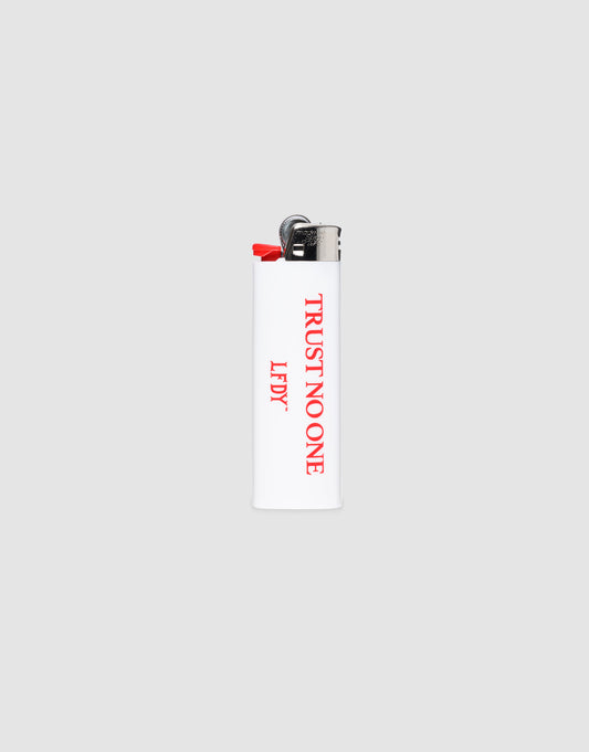 The LFDY Trust No One Lighter by LIVE FAST DIE YOUNG is a white BIC J26 with a chrome cap, red "TRUST NO ONE" on the front, "LEFTY" on the side, and delivers up to 3000 ignitions. Set against a plain light gray background.