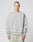 A person with short hair wears the LIVE FAST DIE YOUNG LFDY Wavy Sweater in light gray Oversize Fit, showcasing curved seam details and small white chest text, paired with light gray-green pants against a plain light background.