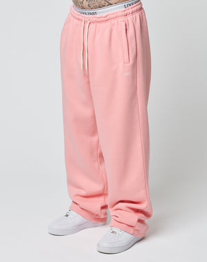 A person wearing LIVE FAST DIE YOUNG Basic Wide Jogger sweatpants in pink with white drawstrings and white sneakers, standing against a plain light background. Only their lower body is visible.