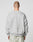 A person with a shaved head is seen from behind, wearing the LIVE FAST DIE YOUNG LFDY Wavy Sweater in light gray, featuring subtle curved stitching and an oversized fit, paired with textured light gray pants. The background is plain and light.