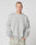 A young man with short hair wears the LIVE FAST DIE YOUNG LFDY Wavy Sweater, a loose light gray Baumwolle sweatshirt with curved stitching and chest text, paired with oversize light gray pants, standing against a plain white background.