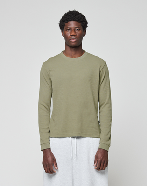 A young man faces forward against a plain light gray background, wearing the LIVE FAST DIE YOUNG Basic Waffle Longsleeve in olive green and light gray sweatpants.