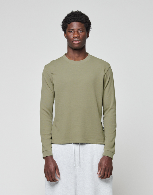 A young man faces forward against a plain light gray background, wearing the LIVE FAST DIE YOUNG Basic Waffle Longsleeve in olive green and light gray sweatpants.