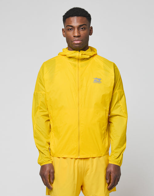 A man faces the camera wearing a bright yellow LIVE FAST DIE YOUNG Live Fast Performance Running Jacket with Kapuze mit Visor and matching yellow shorts. The jacket features a small logo on the left chest, set against a plain light gray background.