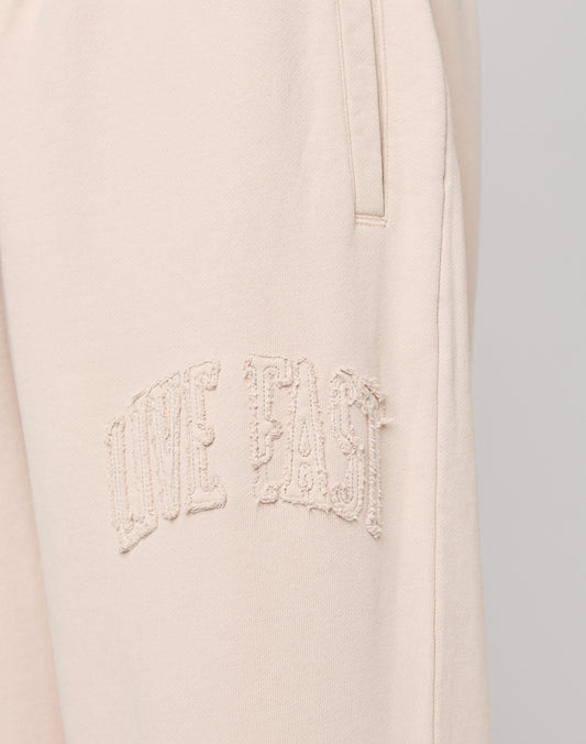 Close-up of Ripped College Wide Jogger by LIVE FAST DIE YOUNG in light beige, crafted from soft Baumwolle, with textured embroidered LIVE FAST text near the pocket.