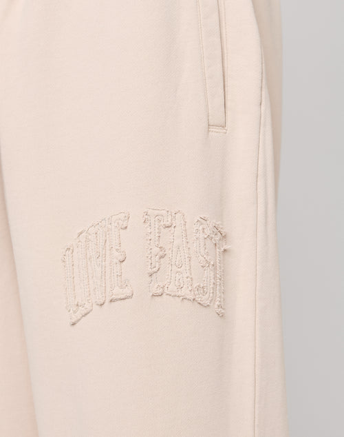 Close-up of Ripped College Wide Jogger by LIVE FAST DIE YOUNG in light beige, crafted from soft Baumwolle, with textured embroidered LIVE FAST text near the pocket.
