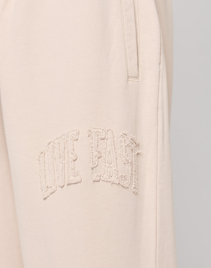 Close-up of Ripped College Wide Jogger by LIVE FAST DIE YOUNG in light beige, crafted from soft Baumwolle, with textured embroidered LIVE FAST text near the pocket.