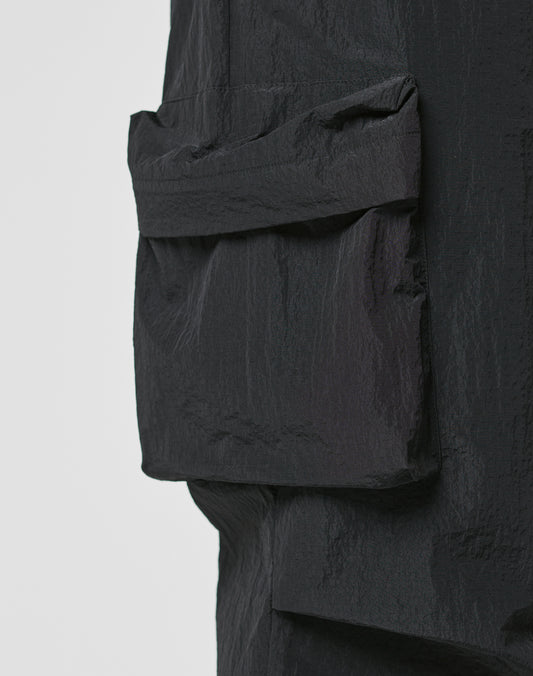 Close-up of textured black fabric with a large rectangular Cargotasche sewn on, part of LIVE FAST DIE YOUNG’s Live Fast Nylon Pants, shown against a plain light background.