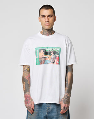 A tattooed man wears the LFDY Sixers Tee from LIVE FAST DIE YOUNG, a white 100% cotton shirt with a colorful two-person car graphic and LIVE FAST text, paired with blue jeans against a plain light background.