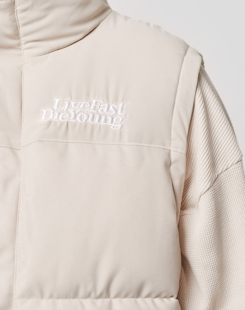 Close-up of the Basic Vest by LIVE FAST DIE YOUNG in beige Regular Fit, featuring white brand embroidery on the left chest, made from soft polyester with a Knopfleiste, worn over a textured, matching long-sleeve top.