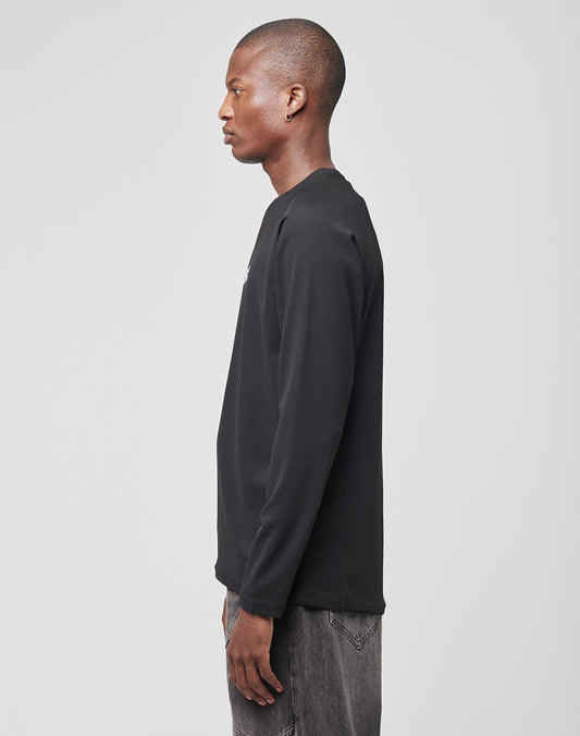A man in profile faces left, wearing a LIVE FAST DIE YOUNG Live Fast Sports Longsleeve (100% Polyester) and gray jeans, standing against a plain light gray background.