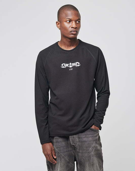A person in a Live Fast Sports Longsleeve by LIVE FAST DIE YOUNG, featuring a stylized white logo and gray jeans, stands against a plain light gray background, looking to the side with one hand in their pocket. Model: LF2310-14898.