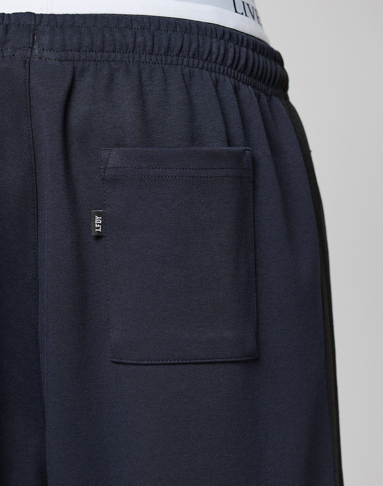 Close-up of the back pocket area of dark navy LFDY Striped Jogger sweatpants by LIVE FAST DIE YOUNG, featuring an elastic waistband and a small black HEY tag. The white waistband of underwear is slightly visible above the pants.