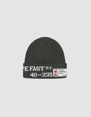 The Live Fast Army Beanie by LIVE FAST DIE YOUNG is a dark gray ribbed knit hat made from 100% Baumwolle, featuring white text and a small frayed web label with numbers and symbols on the folded brim, shown on a plain light gray background.