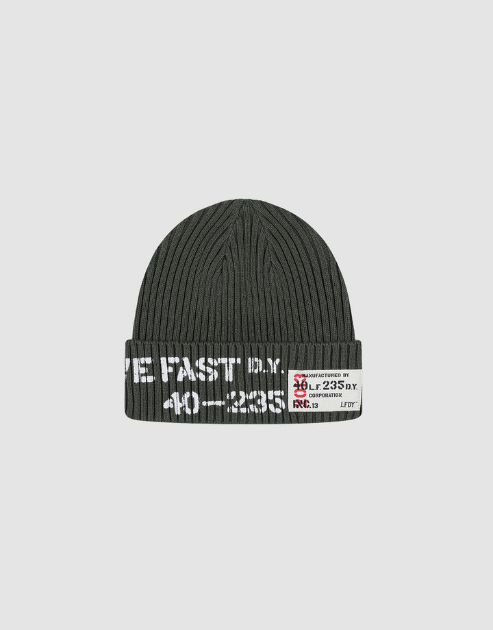 The Live Fast Army Beanie by LIVE FAST DIE YOUNG is a dark gray ribbed knit hat made from 100% Baumwolle, featuring white text and a small frayed web label with numbers and symbols on the folded brim, shown on a plain light gray background. 