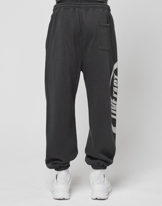 A person wears black LFDY Sphere Jogger pants by LIVE FAST DIE YOUNG, featuring a back pocket, Oversize Fit, and distinctive side logo, paired with white sneakers, standing against a plain white background.