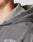 Close-up of a persons neck and shoulder wearing the LFDY Cross Hooded Zip by LIVE FAST DIE YOUNG, featuring LIVE FAST text, layered over a textured light collared shirt. Background is plain and out of focus.