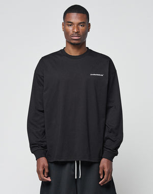 A man faces forward in a LIVE FAST DIE YOUNG Basic Longsleeve—black, loose-fit, with subtle logo text on the left chest—paired with black shorts. The oversize style looks relaxed against a plain light gray background.