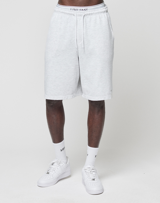 A person models LIVE FAST DIE YOUNG Basic Shorts in regular fit, light gray, knee-length with elastic waistband, paired with white crew socks and sneakers. Only the lower body is shown against a plain white background.