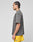 A man with braided hair stands in profile, wearing a faded gray LIVE FAST DIE YOUNG Live Fast Wave Tee with a reflective front print and bright yellow shorts featuring a small logo near the hem, set against a plain light gray background.