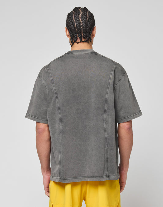 A person with braided hair is seen from the back, wearing the LIVE FAST DIE YOUNG Live Fast Wave Tee in faded gray with an oversize fit, paired with bright yellow shorts, standing against a plain light gray background.