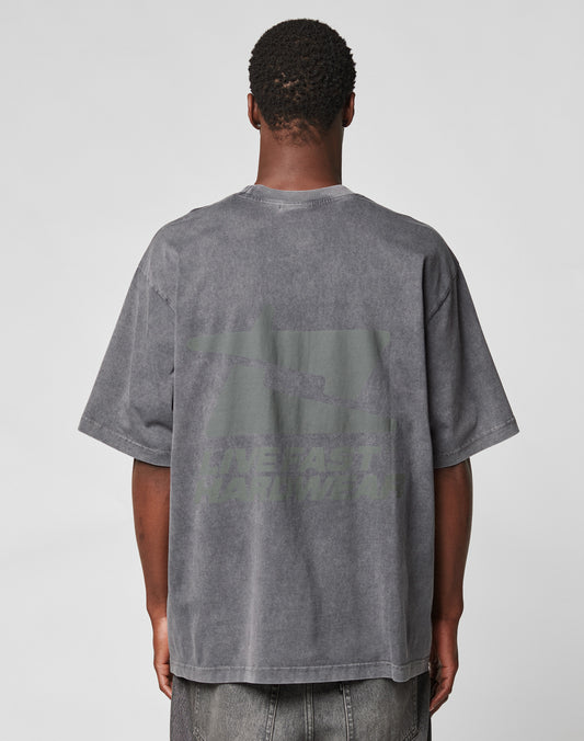 A person with short hair is seen from behind, wearing an oversize fit, faded gray LFDY Hardwear Tee by LIVE FAST DIE YOUNG with subtle front and back prints, paired with gray jeans against a plain white background. | model