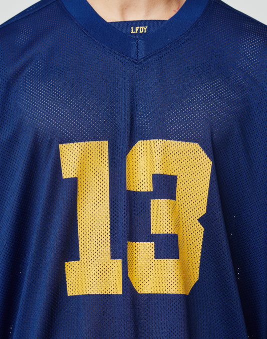 Someone wears the LFDY Mesh Jersey by LIVE FAST DIE YOUNG, featuring an oversize fit, bold yellow number 13 on the front, and LFDY on the V-neckline. Blue mesh fabric completes the sporty look.