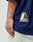 A hand rests beside light-wash jeans, wearing the LIVE FAST DIE YOUNG LFDY Mesh Jersey in navy with an oversize fit and a yellow, black, and white LIVEFAST web patch; initials tattooed on the forearm are also visible.