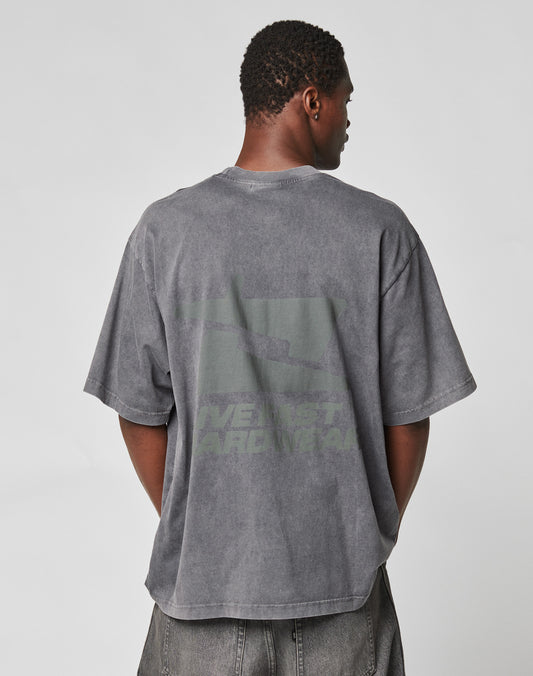 A person with short hair faces away, wearing the LIVE FAST DIE YOUNG LFDY Hardwear Tee—an oversized, faded gray cotton shirt with a subtle back graphic and text—paired with gray pants against a plain, light background.