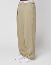 Someone stands against a plain white background wearing LIVE FAST DIE YOUNG Wide Casual Pants in beige with an elastic waistband, paired with white sneakers and a visible white "LIVE FAST" branded waistband. | model