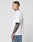 A man with short hair and tattoos on his neck and arm stands in profile wearing the LFDY Triple Racing Tee by LIVE FAST DIE YOUNG—an oversize fit white T-shirt with multilogo frontprint, made from 100% Baumwolle, paired with blue jeans against a gray background.