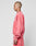 A person with a shaved head and tattoos wears an oversize fit pink Basic LiveFast Sweater by LIVE FAST DIE YOUNG with matching sweatpants, standing in profile against a plain light gray background.
