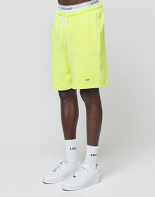 A person wears neon yellow Basic Shorts by LIVE FAST DIE YOUNG with elastischer Bund, white crew socks with “LEDFY” logo print, and white Nike sneakers. Only their lower half is visible, standing against a plain white background.