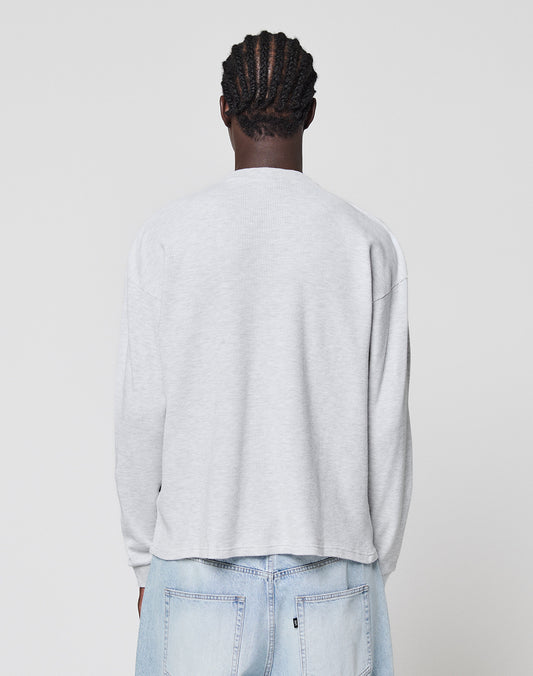 A person with braided hair faces away from the camera, wearing a LIVE FAST DIE YOUNG Blank Waffle Longsleeve in light gray Oversize Fit and light blue jeans against a plain white background.