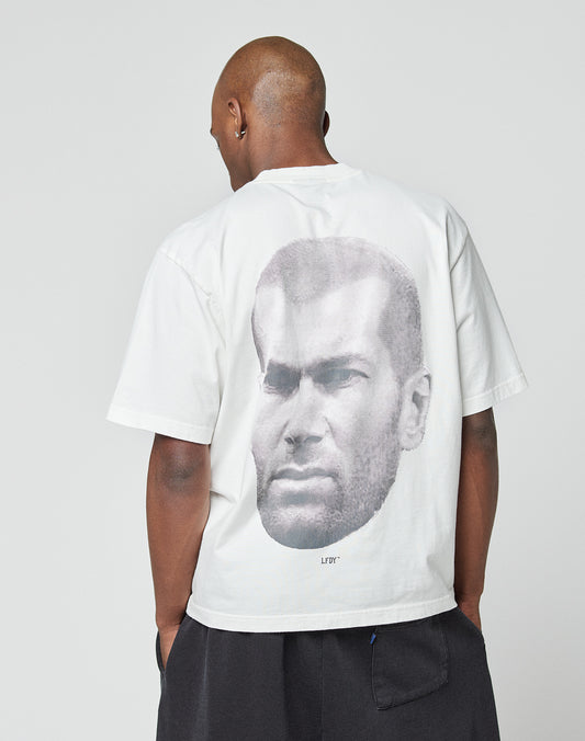 Wearing an oversize fit LFDY Zizou Tee by LIVE FAST DIE YOUNG, featuring 100% cotton and a bold black-and-white close-up portrait as a backprint, the person stands against a plain light background.