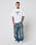 A man with short hair and tattoos wears the LFDY Triple Racing Tee by LIVE FAST DIE YOUNG, an oversized white T-shirt styled with baggy blue jeans and white sneakers, posing against a plain light background.