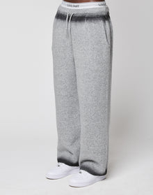Someone wears LIVE FAST DIE YOUNG's Live Fast Boucle Pants—wide fit, light gray, straight leg with elastic waistband labeled "LIVE FAST"—with white sneakers, standing against a plain background.