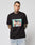 A tattooed man wears the LIVE FAST DIE YOUNG LFDY Sixers Tee, a black regular fit cotton shirt with a graphic of two cartoon people in a car and the words “LIVE FAST,” standing against a plain white background.