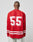 A person with a shaved head wears the LIVE FAST DIE YOUNG LFDY Hockey Jersey—an oversized red polyester top with white stripes and bold “55” print on the back—paired with light-colored jeans, facing away from the camera.
